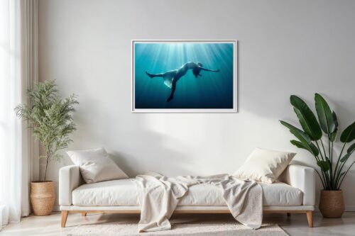 A framed underwater fine art photograph displayed above a sofa in a living room, showing a floating female figure suspended in blue water, illuminated by soft rays of light from above.