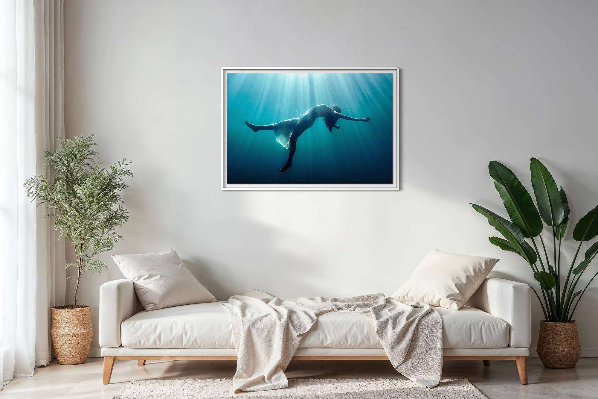 A framed underwater fine art photograph displayed above a sofa in a living room, showing a floating female figure suspended in blue water, illuminated by soft rays of light from above.