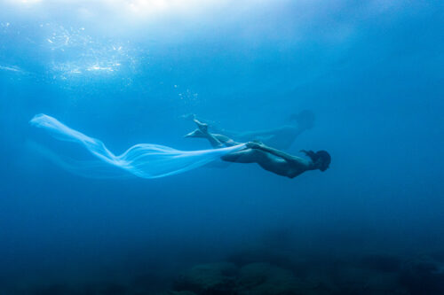 An underwater photo showing a woman holding a veil.