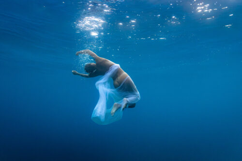 Fine art photo of a woman in water, surrendering and going towards the surface where light and bulbs can be seen.